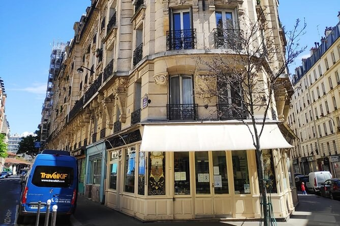 A Haussmann street corner with a café awning and a tour van passing